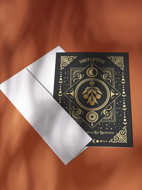 Mistletoe-themed holiday ritual card featuring a gold-stylized mistletoe design with celestial and ornate decorative accents on the front and an inside message explaining the mistletoe's historical significance and its use in Winter Solstice and Twelfth Night rituals for love, protection, and prosperity.